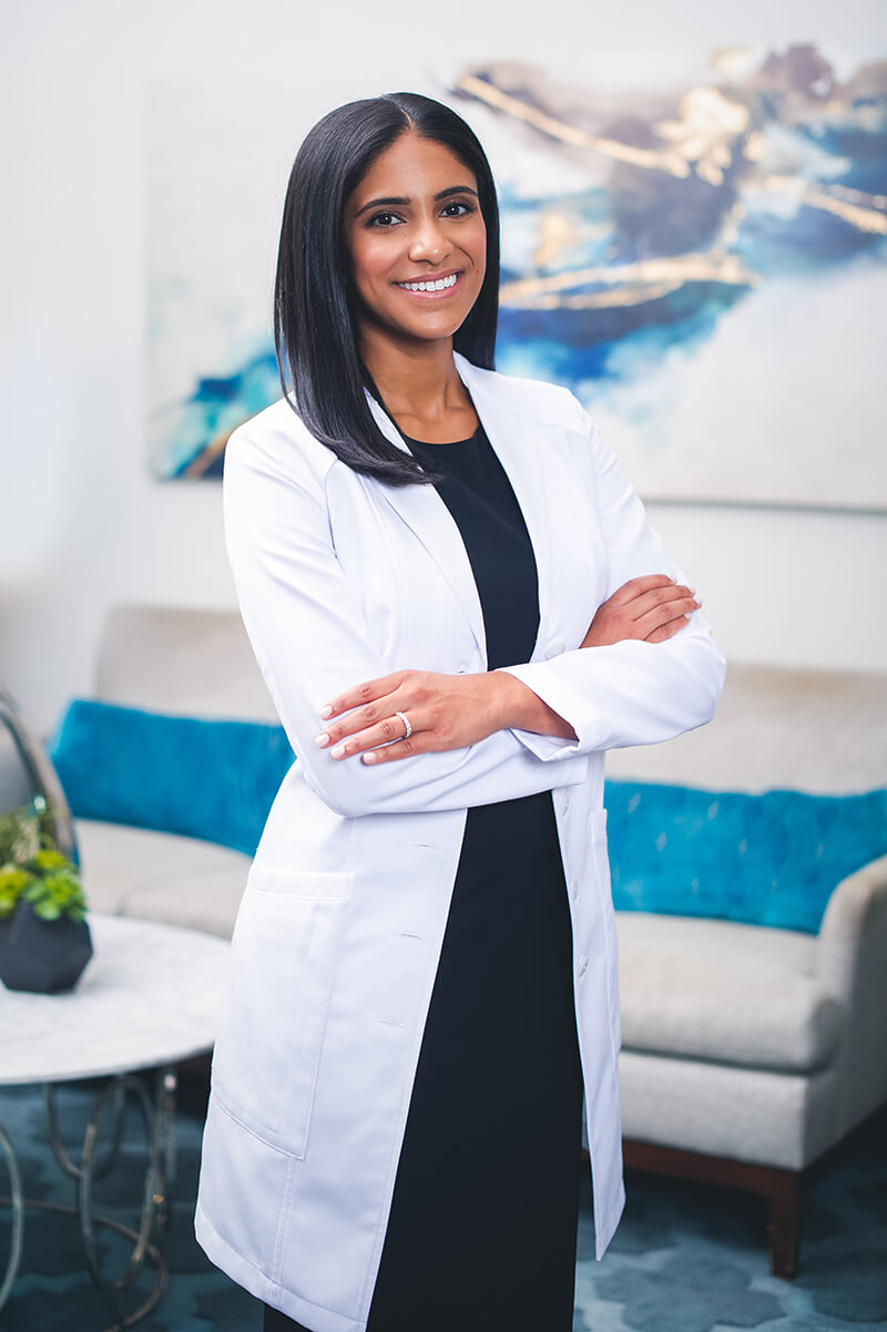 Dr Amy Hassan standing with arms crossed in a white jacket and blue dress