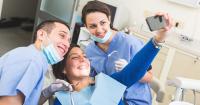 Female dental patient taking a selfie with male and female dental professionals